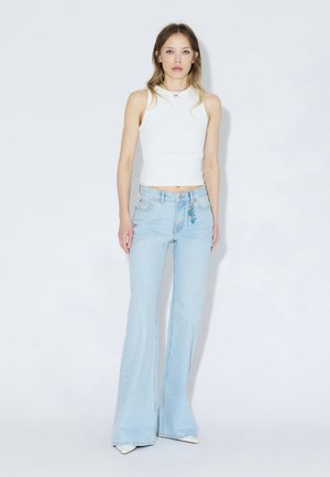 Valkoinen hihaton paita yhdistetty vaaleansinisiin levenevään farkkuihin, joissa on sininen koriste vyölenkillä. Sileä kangas ja istuva malli.