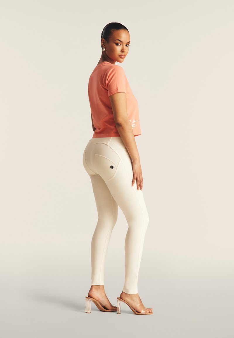 Top corto rosa, leggings blancos ajustados y sandalias de tacón transparentes. Tejido texturizado con costuras visibles y detalles de bolsillos en los leggings.