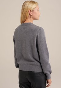 Szürke kötött pulóver kerek nyakkivágással, bordás mandzsettával és szegéllyel, puha anyagból készült, fekete bőr nadrággal párosítva.