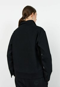 Svart oversized sweatshirt med hög krage, har långa ärmar och sprund vid manschetterna. Tillverkad av ett mjukt, strukturerat tyg.