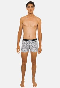 Boxers pour hommes en tissu extensible, avec une ceinture noire portant le logo "WAXX" et de petits motifs noirs à pois sur un fond blanc.