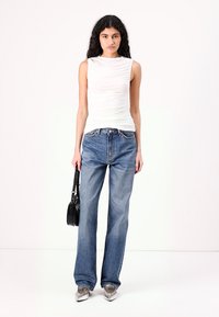 White sleeveless top with a ruched texture, paired with loose blue jeans. Model holds a small black handbag, wearing silver shoes.