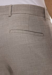Hellbraune Hose aus strukturiertem Stoff, mit einer flachen Gesäßtasche und einem glatten Bund. Schlichtes, tailliertes Design ohne sichtbare Beschläge.