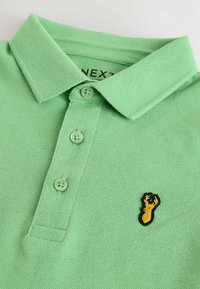 Zelená polo tričko vyrobené z texturovanej látky, so žebrovaným golierom, tromi gombíkmi a žltým logom homára na ľavej hrudi.