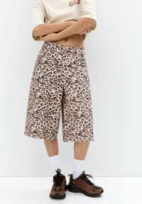 Culoare bej cu imprimeu leopard, pantaloni scurți culotte cu croială lejeră, realizați dintr-un material moale. Asortați cu pantofi sport maro și negri și șosete albe.