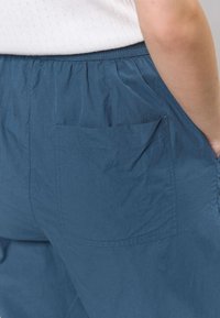 Plave lagane hlače od tkanine s elastičnim pojasom i bočnim džepom. Tekstura izgleda glatko s minimalnim nabora.