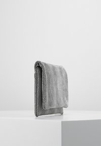 Szara teksturowana torba z klapą na zakładkę, wykonana z materiału przypominającego siatkę, o kompaktowym, prostokątnym kształcie, wyeksponowana na białym tle.