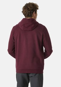 Burgundská mikina s kapucí na stahování a žebrovanými nároky. Vyrobená z měkké tkaniny, má uvolněný střih a rovný lem.