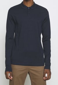 Marinblå långärmad pikétröja i bomull, med klassisk krage, treknappars stängning och subtila sömnadsdetaljer.