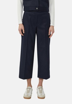 Marineblauwe, met krijtstreepjes, wijd uitlopende cropped broek gecombineerd met een wit shirt met lange mouwen en witte sneakers met beige accenten.