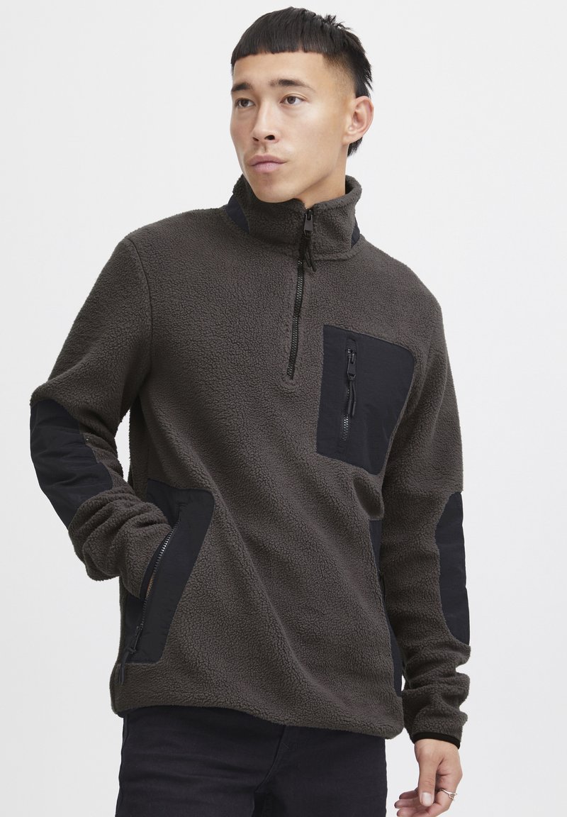Fleece-Pullover in Dunkelgrau mit hohem Kragen, Reißverschlusstasche auf der Brust und schwarzen Stoffakzenten an den Schultern und Seitentaschen.