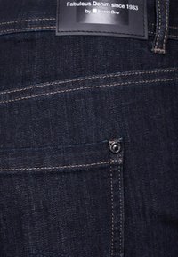 Mörkblå denimjeans med en standard femficksdesign, synlig sömnad, stängning med metallknapp och en svart tyglapp sydd i linningen.