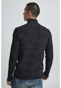 Dunkellila strukturierter Pullover mit hohem Kragen und geripptem Saum, getragen mit blauen Jeans, die ein lässiges und figurbetontes Design aufweisen.