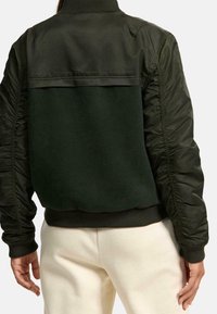 Groene bomberjack met een wollen achterkant en glanzende nylon mouwen. Kenmerkt zich door een geribde kraag en boorden, en heeft een relaxte pasvorm.