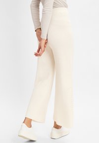 Weite Hosen in cremefarbenem Rippstrick mit hohem Bund, die eine gerade Silhouette und seitliche Schlitze am Saum aufweisen.