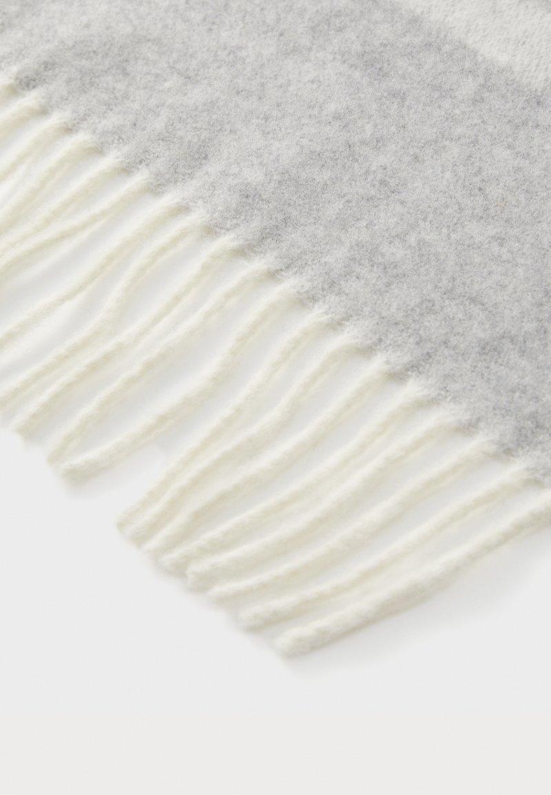 Écharpe en laine grise avec une texture douce, ornée de franges blanches le long du bord inférieur. Le design présente un effet d'ombrage en dégradé.