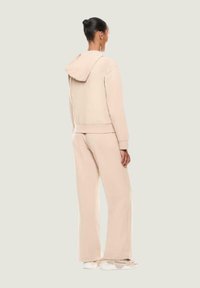 Sudadera color beige y pantalones anchos a juego, fabricados en tejido suave; cuenta con capucha, puños acanalados y un corte relajado.