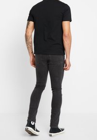 Černé tričko v kombinaci s tmavě šedými slim-fit džíny a černými vysokými teniskami, které mají bílé detaily a klasické švy.