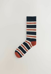 Striped sock with navy blue, white, and rust patterns. Features a solid rust-colored toe and heel. Made from a soft, stretchable material.