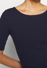 Granatowa bluzka z krótkim rękawem, wykonana z gładkiego, elastycznego materiału, z okrągłym dekoltem i dopasowanym krojem. Bez widocznych wzorów ani ozdób.