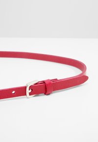 Rød lærbelte med et tynt design, sølvfarget metallspenne og en løkke for justering. Teksturet overflate, avsmalnende ender.