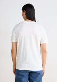 Hvit bomull T-skjorte med korte ermer og rund hals, kombinert med blå denimjeans. Glatt tekstur, enkel design og ingen synlige mønstre.