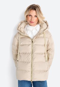 Beige pufferjack met een capuchon, vooraan een rits en een verticale gestepte design. Bevat verstelbare banden en twee zijzakken. Heeft een soepele textuur.