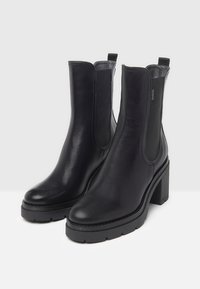 Bottes noires en cuir à la cheville avec des panneaux latéraux élastiques, un talon bloc texturé et un bout rond. Couture de détail le long de la semelle.