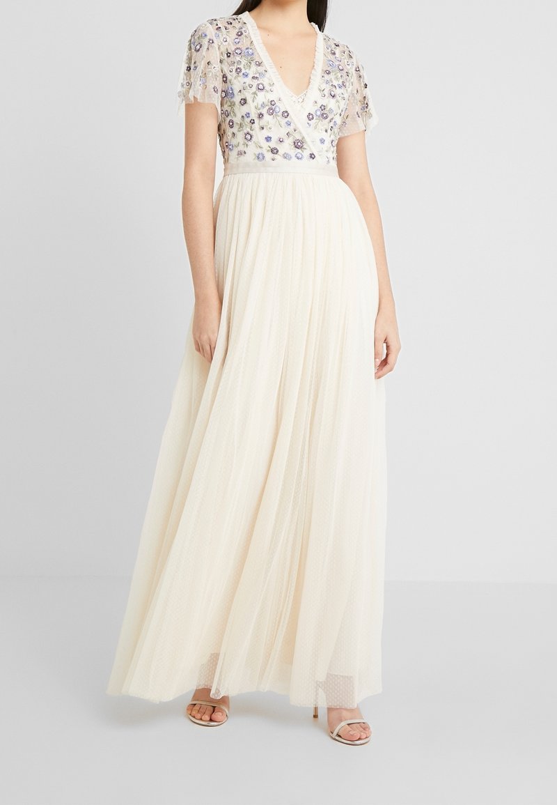 Maxikleid in Creme mit V-Ausschnitt, kurzen bestickten Ärmeln und floralen Verzierungen. Fließender Tüllrock mit geschichteter Textur.