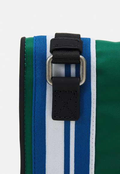 Geantă din material textil verde cu accesorii negre, având dungi verticale albastre și albe. Detaliul notabil include o curea cu clips metalic și accente cusute.