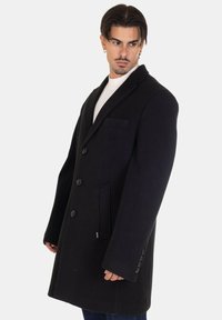 Cappotto di lana nero con un design lungo, rever a notche, chiusura monopetto con cinque bottoni e tasca sul petto.