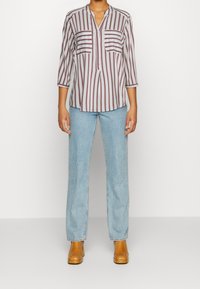 Camicia a righe, con bottoni, di colore grigio chiaro e borgogna, con due taschini sul petto e maniche a tre quarti. Abbinata a jeans azzurri e stivali marroni.
