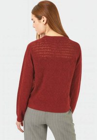 Maglione in maglia rosso scuro con un motivo a diamante, caratterizzato da un retro testurizzato e maniche lunghe. Abbinato a pantaloni a strisce grigie.