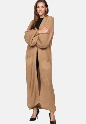Cardigan lungo e aperto di colore cammello, in tessuto a maglia testurizzato, con due tasche frontali e maniche ampie. Indossato sopra un top nero.