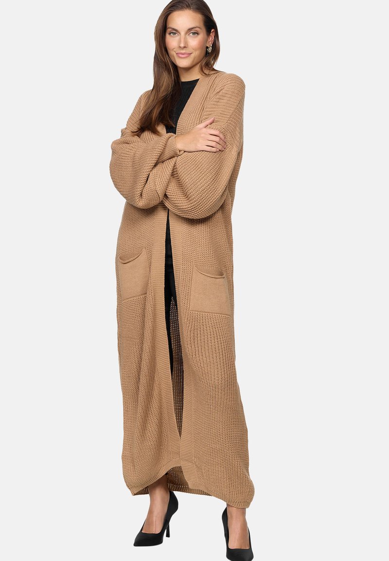 Lång, öppen cardigan i camel-färg, med strukturerad stickad tyg, med två framfickor och vida ärmar. Bärs över en svart topp.