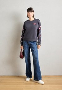 Felpa grigia con maniche a motivo floreale, scollatura rotonda e piccolo design a forma di cuore. Abbinata a jeans svasati blu e sneakers bianche.