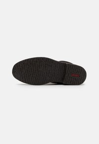 Suola di scarpa in gomma nera con un motivo di grip testurizzato e un logo rosso prominente. Il design è piatto con una punta curva e un bordo liscio.