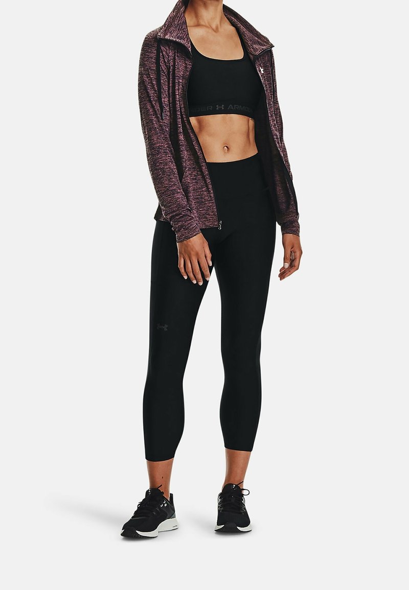 Zwarte sportieve crop top en high-waisted legging met een gestructureerde donkerpaarse zip-up jack. Zwarte sneakers maken de outfit compleet.