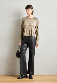 Beige, long-sleeve, button-up blouse with gathered waist; paired with black leather wide-leg pants and black shoes; small handbag.