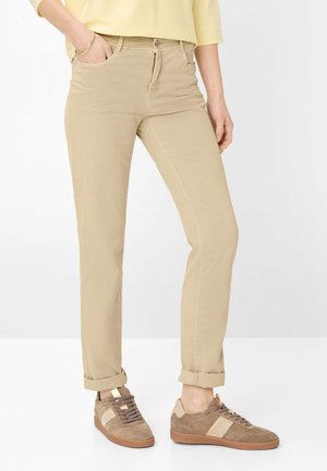 Person wearing beige straight-leg pants with cuffed hems, yellow top, and brown suede sneakers with beige stripes.