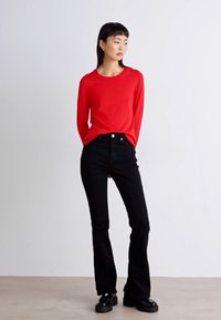 Κόκκινο πουκάμισο με μακριά μανίκια συνδυασμένο με ψηλόμεσα μαύρα τζιν. Τα τζιν έχουν φαρδιά γραμμή και μαύρα παπούτσια με χοντρή σόλα. Λείο υλικό.