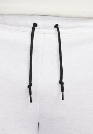 Pantalones de chándal blancos con tejido texturizado, con un cordón negro y punteras metálicas, y detalles visibles en la cintura.