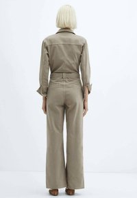 Combinaison en denim beige à manches longues, col et pantalon large. Présente une taille ajustée et des poignets roulés pour un look décontracté.