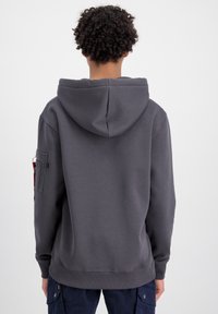 Felpa grigia scura con ampio tascone a marsupio e cappuccio regolabile con cordino. Presenta una tasca laterale con chiusura a zip. Cuffs e orlo elastici.