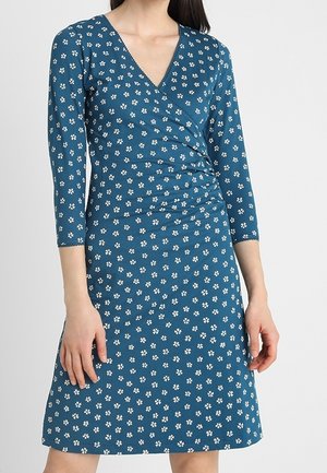 V-neck dress in teal with three-quarter sleeves, featuring a gathered waist and white floral patterns on the fabric. Smooth, stretchy material.