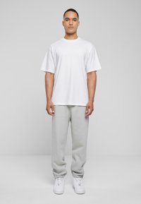 White crew neck t-shirt with short sleeves, paired with light gray sweatpants and white sneakers. Simple, relaxed fit without patterns.