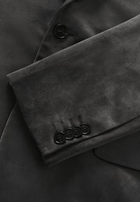 Melna samta žaketes piedurkne ar gludu tekstūru, kurai ir melna poga un četras dekoratīvas pogas pie aproces.