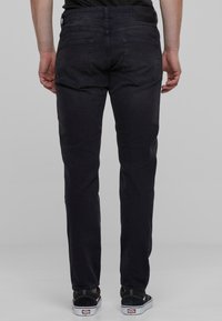 Vaqueros de mezclilla oscura con corte slim, que cuentan con cinco bolsillos y una cintura de altura media. El diseño incluye un desgaste sutil y detalles de costura.
