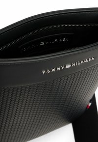 Sort struktureret lædertaske med et vævet design, som har en lynlåslukning og sølvfarvet logo-tryk fra Tommy Hilfiger.