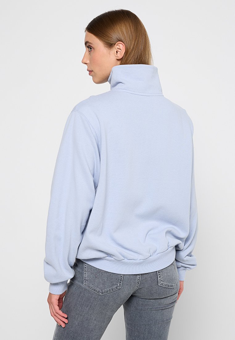 Sweatshirt bleu clair avec un col haut, un ourlet élastique et des manches longues. Texture douce et coupe décontractée. Aucun motif ou logo visible.